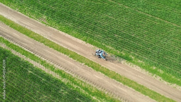 Fototapeta Aerial view of a cyclist on a bicycle riding on a country road between green fields. Cycling traveler riding across the field on a dirt road.