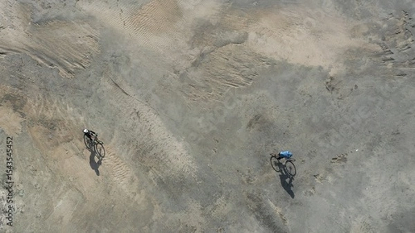 Fototapeta Aerial view of man and woman on bikes riding through the desert on a bright sunny day.