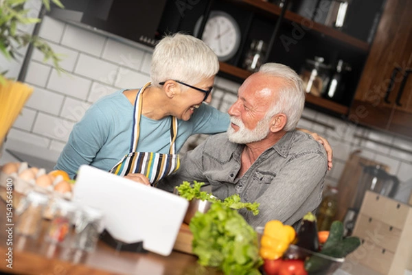 Obraz Mature couple following recipe on digital tablet while preparing lunch in the kitchen