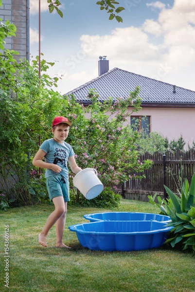 Obraz A little boy, vacationing in his grandmother's garden during the summer, prepares a small outdoor pool for swimming and refreshing himself in the cold water