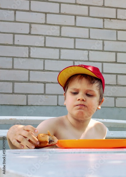 Obraz A little boy takes a big bite of a bun, his mouth full, his cheeks puffed out