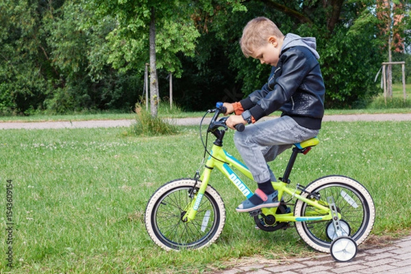 Obraz A little boy is learning to ride a bike, he concentrates on pedaling