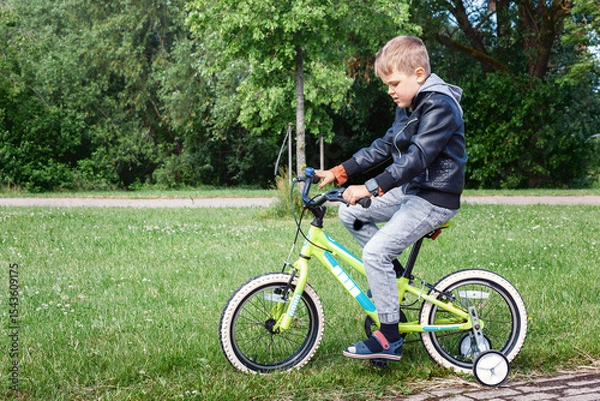 Obraz A little boy wearing a black jacket riding a yellow bicycle with white wheels