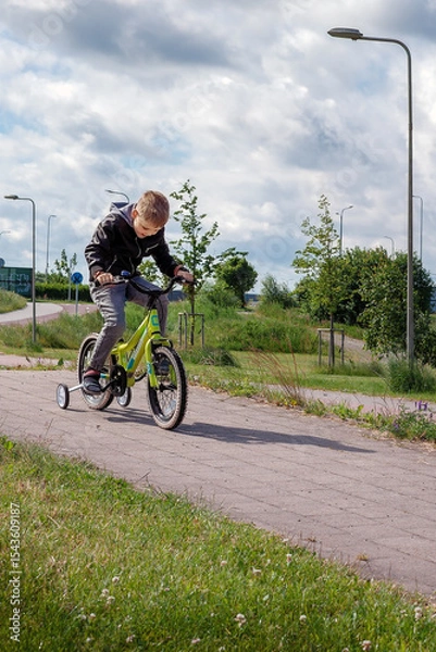 Obraz A little boy is riding his bike down a hill in the park