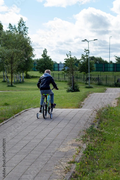 Obraz A little boy in a black jacket rides a bicycle on a mountain path in the park. View from behind