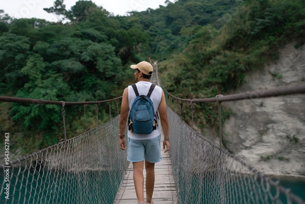 Obraz Man crosses a suspension bridge in a lush green landscape