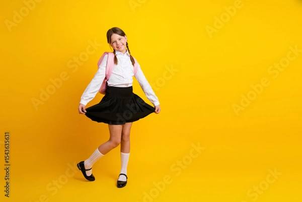 Obraz Adorable schoolgirl smiling in formal uniform against a bright yellow background, celebrating back-to-school season with joy