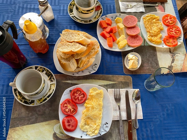 Fototapeta Breakfast in hotel series. Top view of healthy breakfast spread at homestay or guesthouse. Eggs, fresh fruits, bread tea and juice. Cozy, rustic setting, dining, or food concept. Trinidad, Cuba.