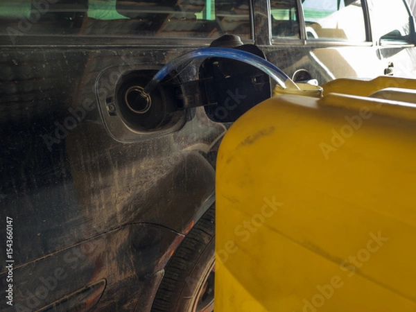Obraz Large yellow container pours fuel into car's tank with clear tube. Practical scene captures outdoor setting and utilitarian mood of fueling process.