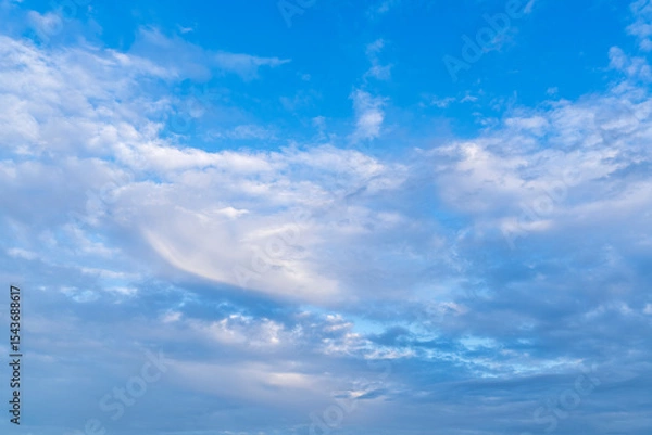 Fototapeta Clouds float gently across a serene blue sky tinted with the soft hues of sunset, creating a tranquil and dreamy evening atmosphere.