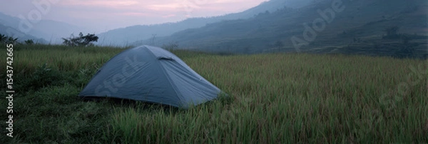 Fototapeta Tent set up in serene rice field at dusk, surrounded by misty mountains