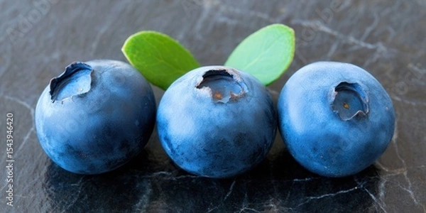 Obraz Three ripe blueberries sit on a dark, textured surface, perfect for a healthy snack.
