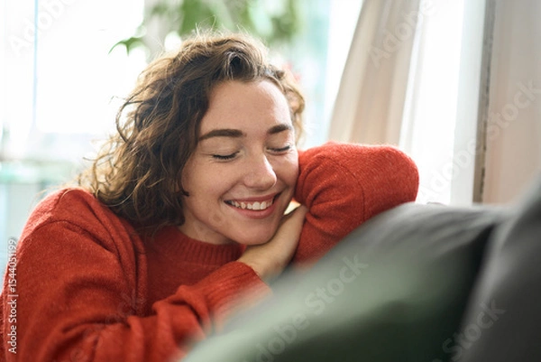 Obraz Young smiling pretty curly woman relaxing sitting on couch at home and chilling. Happy relaxed calm beautiful lady enjoying peace of mind and comfort of soft new sofa with eyes closed. Close up.