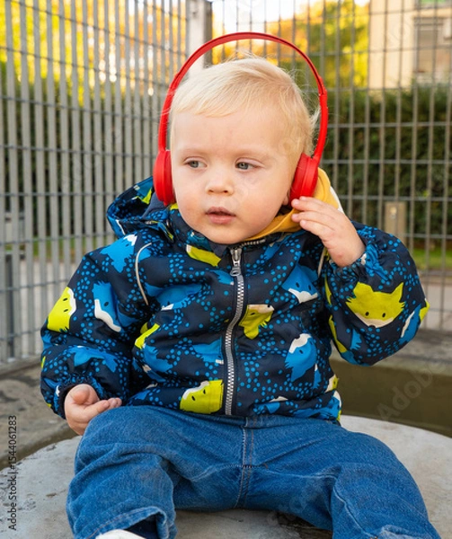 Fototapeta A young child wearing headphones and a blue jacket