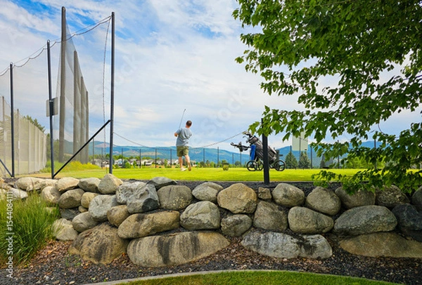 Fototapeta A young man holds the finish after a swing at a suburban golf course.