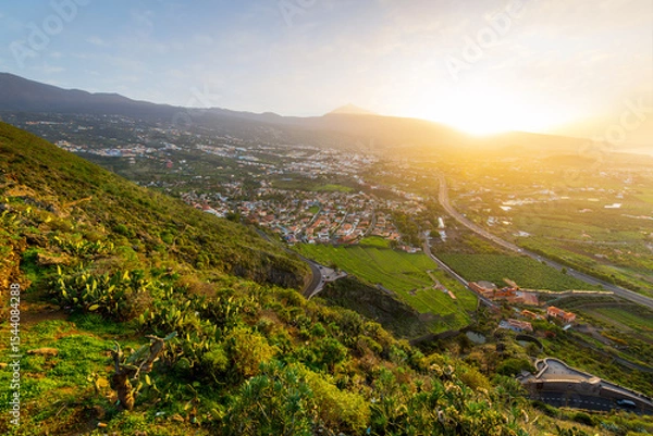 Fototapeta View from the Mirador de Humboldt lookout of the Orotava Valley towns of Puerto de la Cruz, La Orotava and Los Realejos, with Mt Teide volcano in the distance, Tenerife Island, Spain at golden hour.