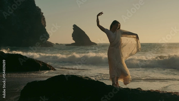 Fototapeta A girl in a sari dances against the backdrop of the ocean at sunset. Meditation.  Yoga. Soft focus