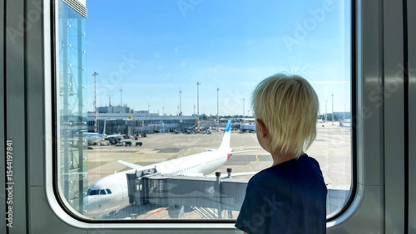 Fototapeta Horizontal portrait of Little blond boy looking out of the window in airport and curious watching transportation system. Toddler enjoys traveling with airplane and vacation.