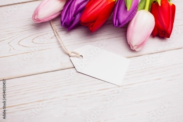 Obraz Flat design is showing tulip blossoms resting on pale wooden tabletop with blank white gift tag