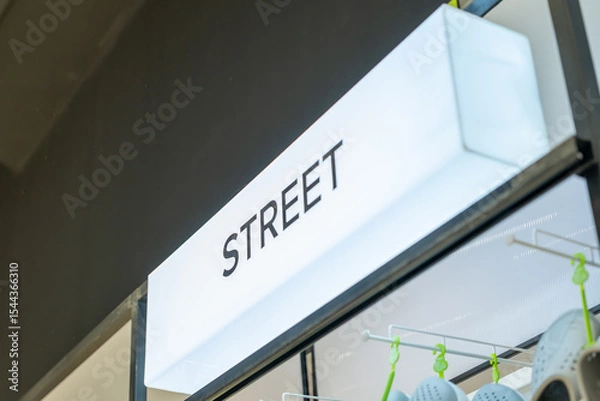 Fototapeta Close-up side angle of an illuminated white retail sign with the word "STREET" above a footwear display in a modern store interior.