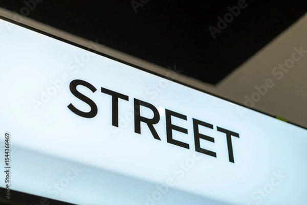 Fototapeta Close-up side angle of an illuminated white retail sign with the word "STREET" above a footwear display in a modern store interior.