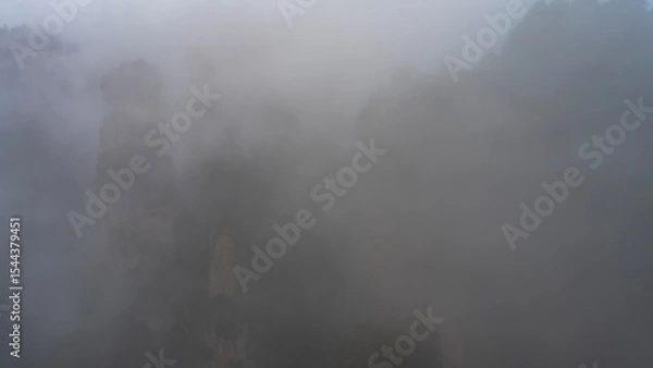 Fototapeta A mystical misty landscape. The high pillars mountains are shrouded in thick fog. The outlines of the rocks are barely visible through the haze. Poor visibility. China.Zhangjiajie National Forest Park