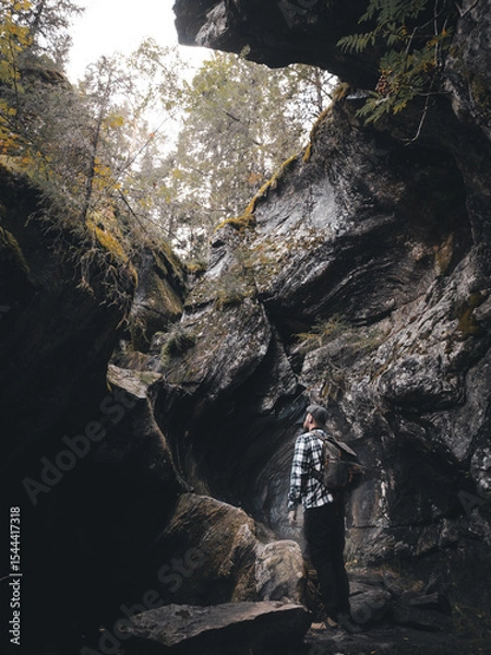 Fototapeta A man stands at the bottom of a massive, split giant’s kettle—an impressive natural rock formation at Pumpulikirkko in Rautavaara, Finland. Towering rock walls surround the narrow crevice.