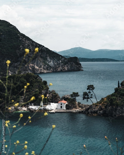 Fototapeta A close-up view of the charming white chapel with a red roof on Panagia Island, just off the coast of Parga, Greece. The turquoise Ionian Sea surrounds the small island.