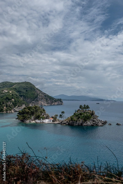 Fototapeta Idyllic view of Panagia Island with its small white chapel and lush greenery, located off the coast of Parga in the Ionian Sea. The scenic landscape combines turquoise water, dramatic cliffs