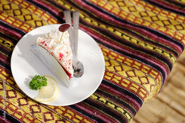 Fototapeta Homemade fresh strawberry cheese cake with lemon piece in white dish on Thai native pattern tablecloth in natural sunlight in tropical cafe