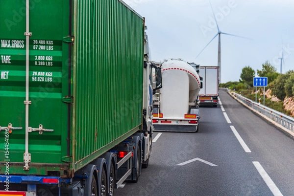 Fototapeta Several trucks in a row overtaking on a highway, merging into the left lane.