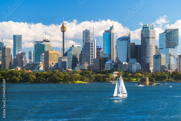Fototapeta Beautiful Sydney city skyline panorama with tower and modern skyscrapers viewed across the harbour from Bradleys Head with blue sky and white fluffy clouds on a day