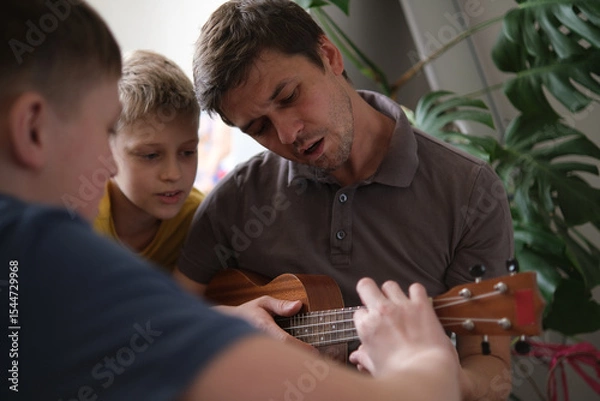 Fototapeta Happy father and sons playing guitars together and smiling at home