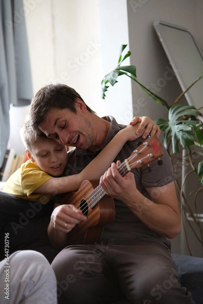 Fototapeta Father teaching son ukulele, smiling and bonding warmly at home
