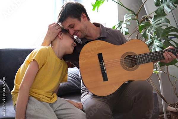 Fototapeta Father and son hugging warmly while playing guitar at home, enjoying music