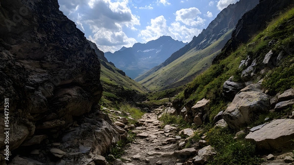 Obraz A narrow trail winding through rocky terrain, with a steep drop-off to one side and distant mountain peaks visible.
