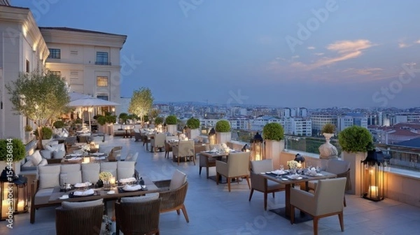 Fototapeta Rooftop with dining tables arranged under hanging lamps, city backdrop at dusk