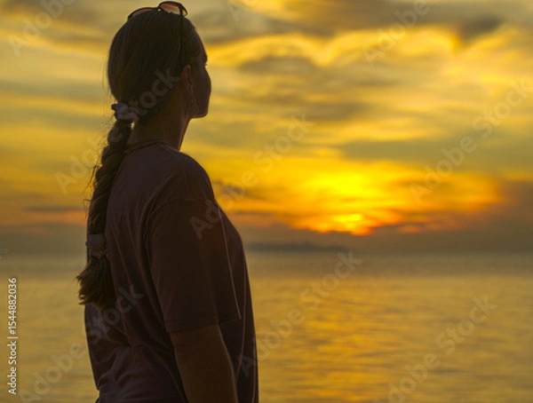 Obraz Woman with Braided Hair Looking at the Sunset Over the Ocean from the Beach Captured from Side Angle with Warm Lighting