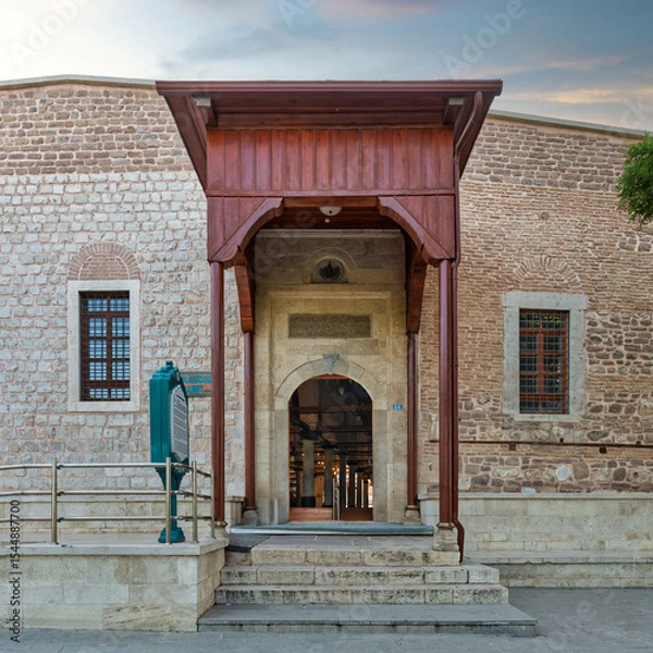 Fototapeta Entrance of Alaaddin Keykubad Mosque, where the intricate stonework and wooden elements reflect the rich history of Konya, Turkey, bathed in soft evening light