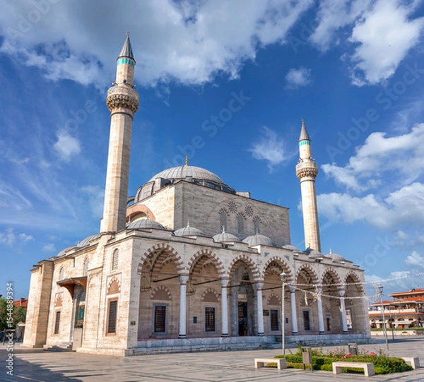 Fototapeta The historic Selimiye Mosque, a 16th-century Ottoman landmark in Konya, Turkey. The building features two minarets and domes, viewed from the square under a blue sky with clouds