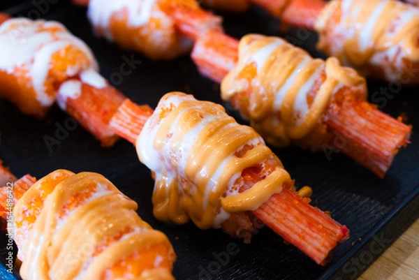 Fototapeta A imitation crab sticks topped with creamy mayonnaise and spicy sauce, arranged neatly on a black serving tray for Japanese-style appetizer or sushi.