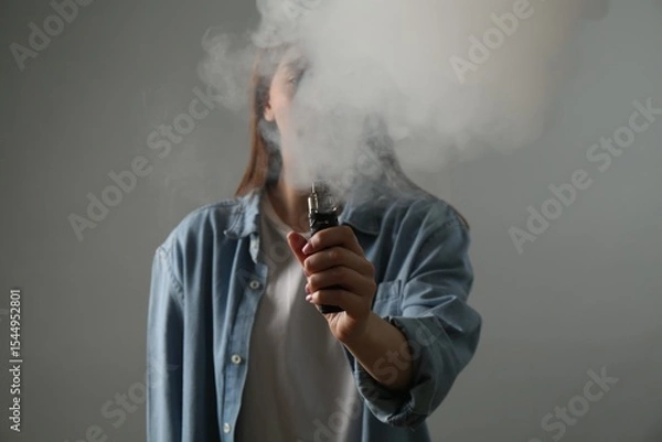 Fototapeta Woman using electronic smoking device on grey background
