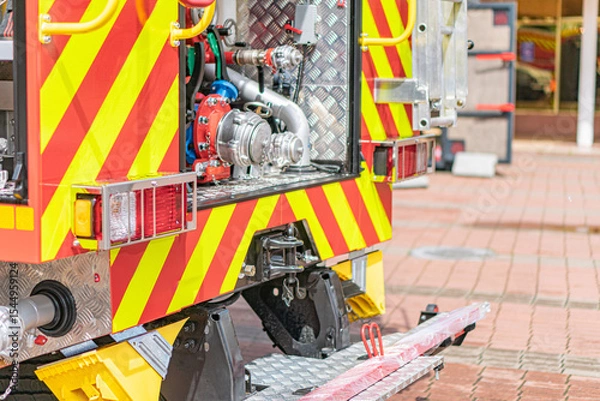 Fototapeta Image of a yellow and red fire truck on a brick roadway, equipped with reflective markings and a large pump