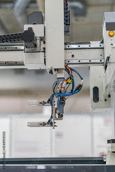 Fototapeta Close-up view of an industrial robot, predominantly white, grey, and black in color, with visible wires and cables No people present Even lighting without harsh shadows Standard photograph style