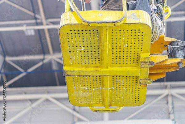 Fototapeta Large yellow machinery on a warehouse floor, industrial tower truck with multiple holes, concrete backdrop, fluorescent lighting, crane system or platform, cables, mechanical components, operational