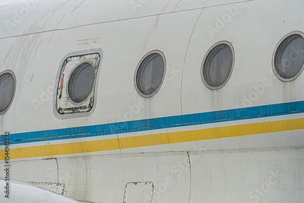 Fototapeta Large white and blue-orange striped jet airplane on airport tarmac, visible engines, open front door revealing interior lighting, no identifying marks