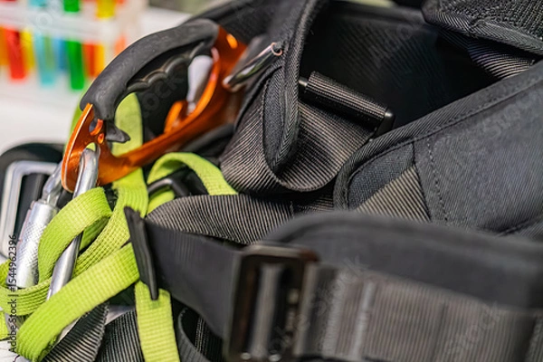 Fototapeta Black backpack containing mountaineering gear, including orange safety goggles and a dark electronic device, located in an indoor setting with multiple straps and compartments