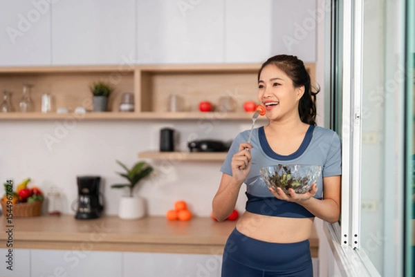 Obraz ESG and Healthy Choices. Smiling woman with a salad by the window in a bright kitchen.