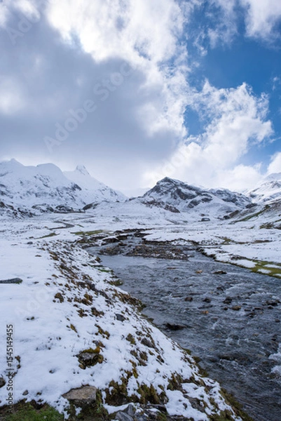 Fototapeta Snowy mountain landscape with a clear stream flowing through a valley under a partly cloudy sky