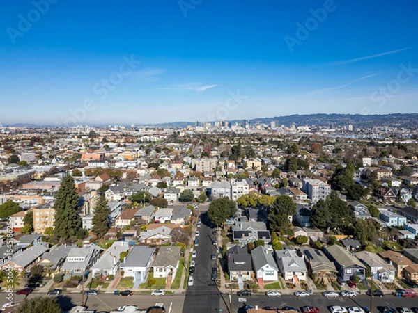 Obraz Aerial view of a suburban residential area in Alameda with streets, houses, and distant city skyline under clear blue sky, panoramic urban neighborhood scenery, residential community living concept